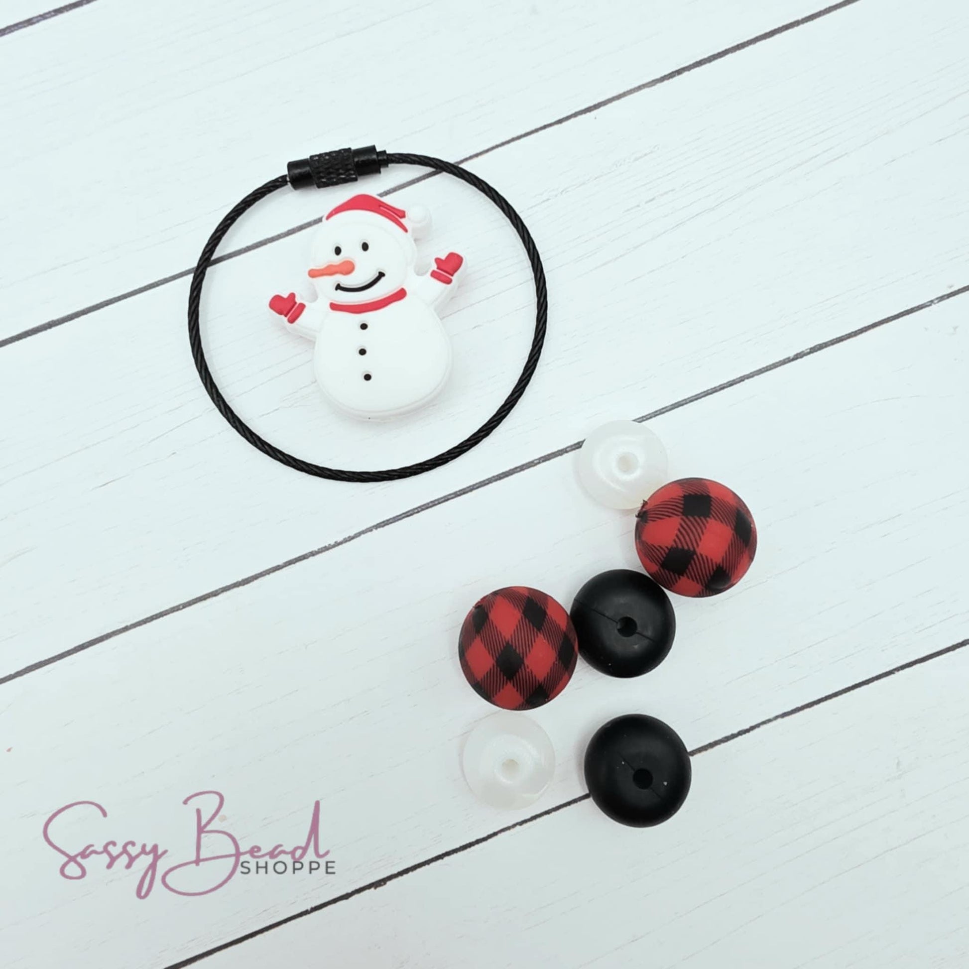 Snowman styled flat lay showing beads for tumbler charm, including seasonal snowman and black & red plaid bead designs