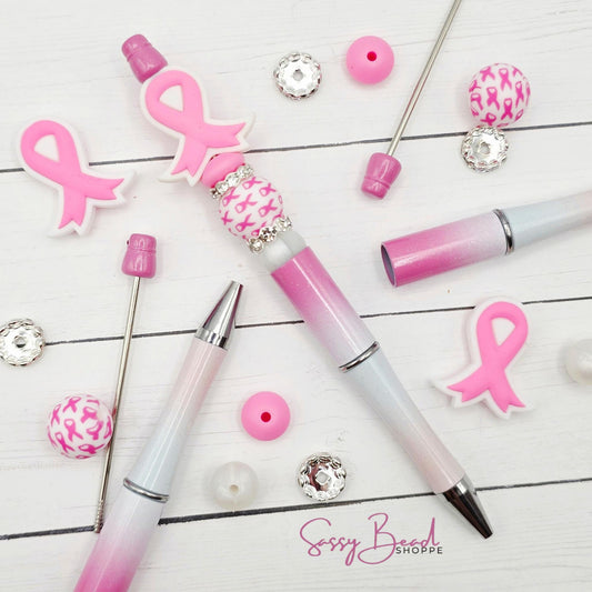 Brave In Every Stroke close-up of breast cancer awareness -themed silicone beads in pink ribbon designs for DIY pen making