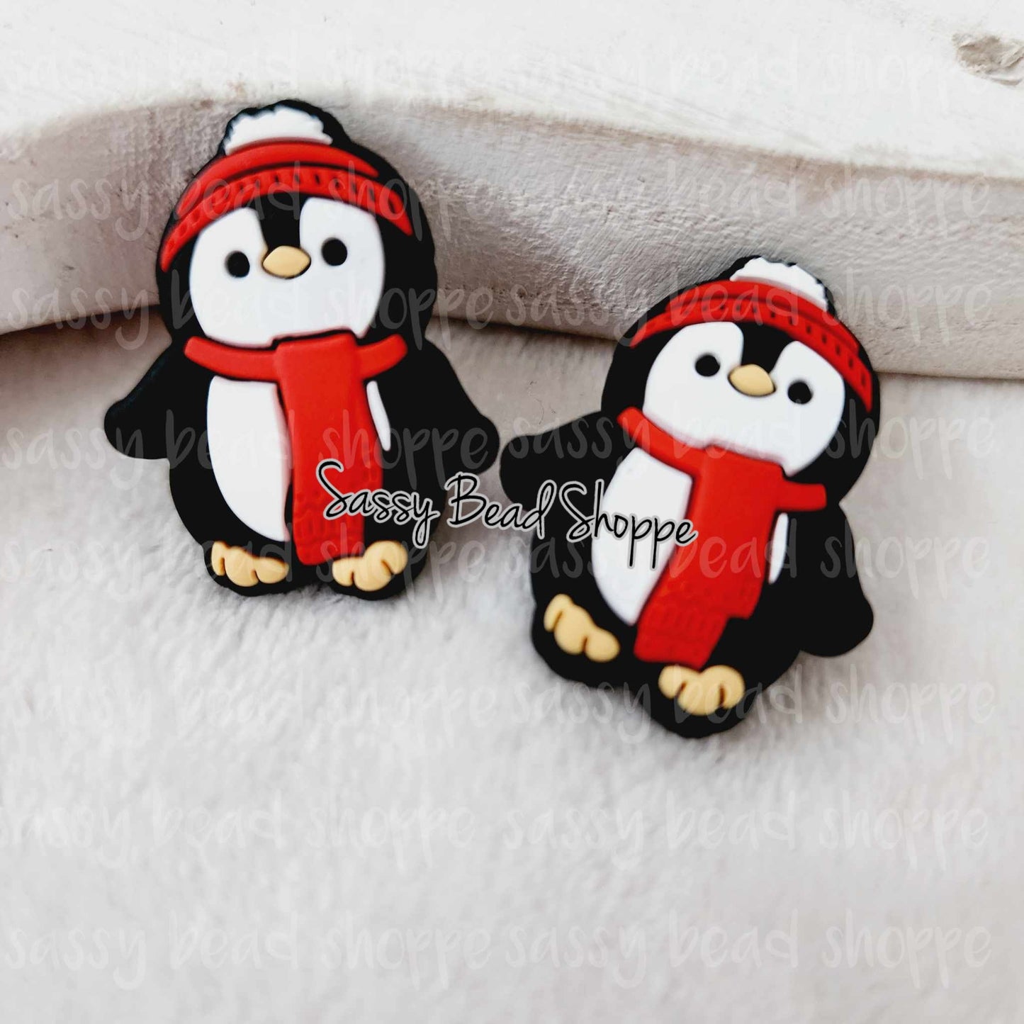 May include: Two black and white penguin charms with red scarves and white hats. The charms are made of silicone and are approximately 1 inch tall.