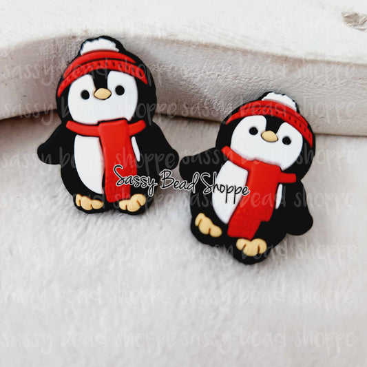 May include: Two black and white penguin charms with red scarves and white hats. The charms are made of silicone and are approximately 1 inch tall.